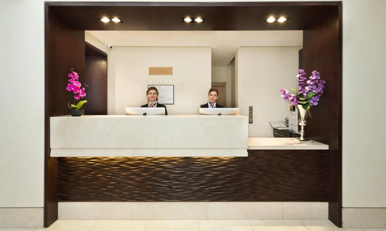 two people sitting at a reception desk in front of a mirror at The Park City Grand Plaza Kensington Hotel in London
